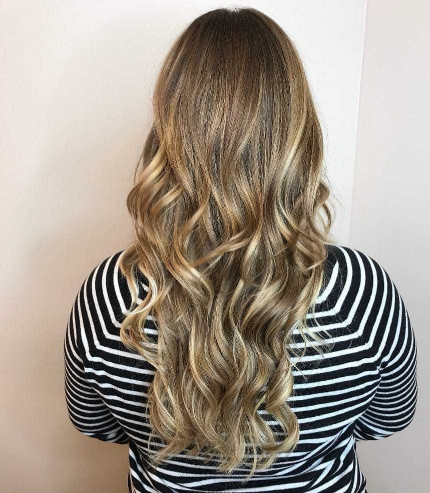 Long, wavy blonde hair with dark roots, worn by person in a black and white striped shirt.