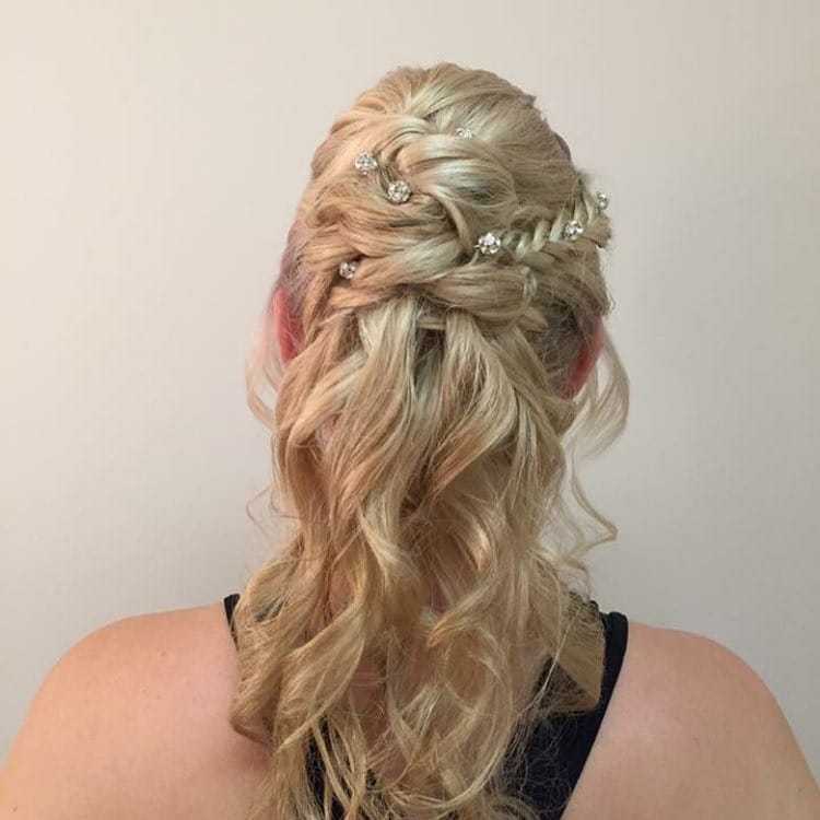 Intricate braided hairstyle with decorative pins on wavy blonde hair.
